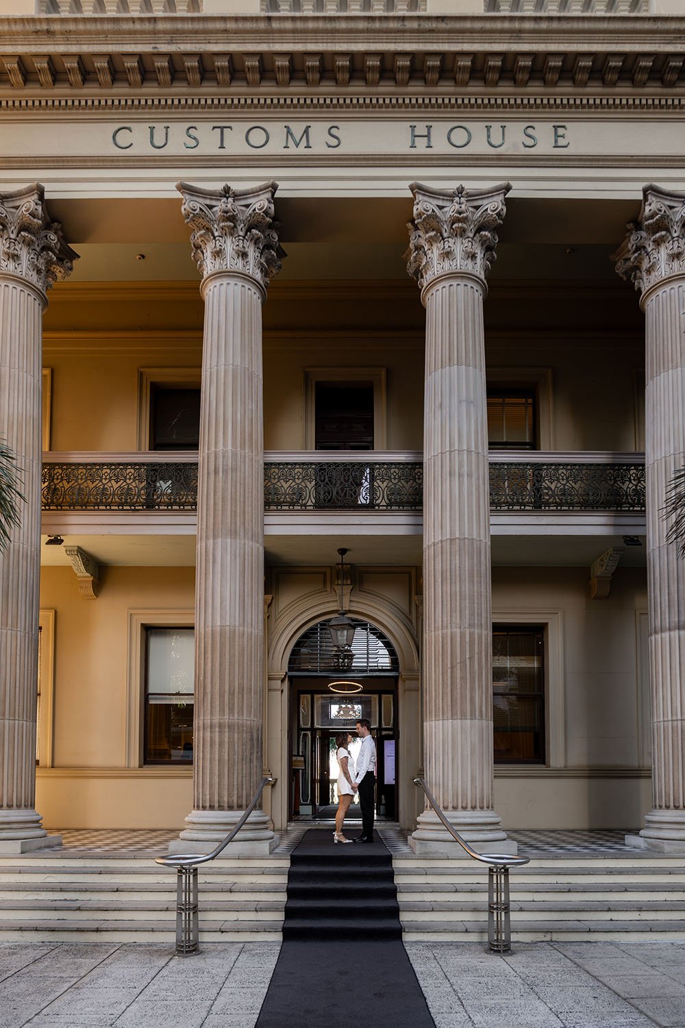 Brenna and Morgan holding hands look at each other in front Customs House Brisbane