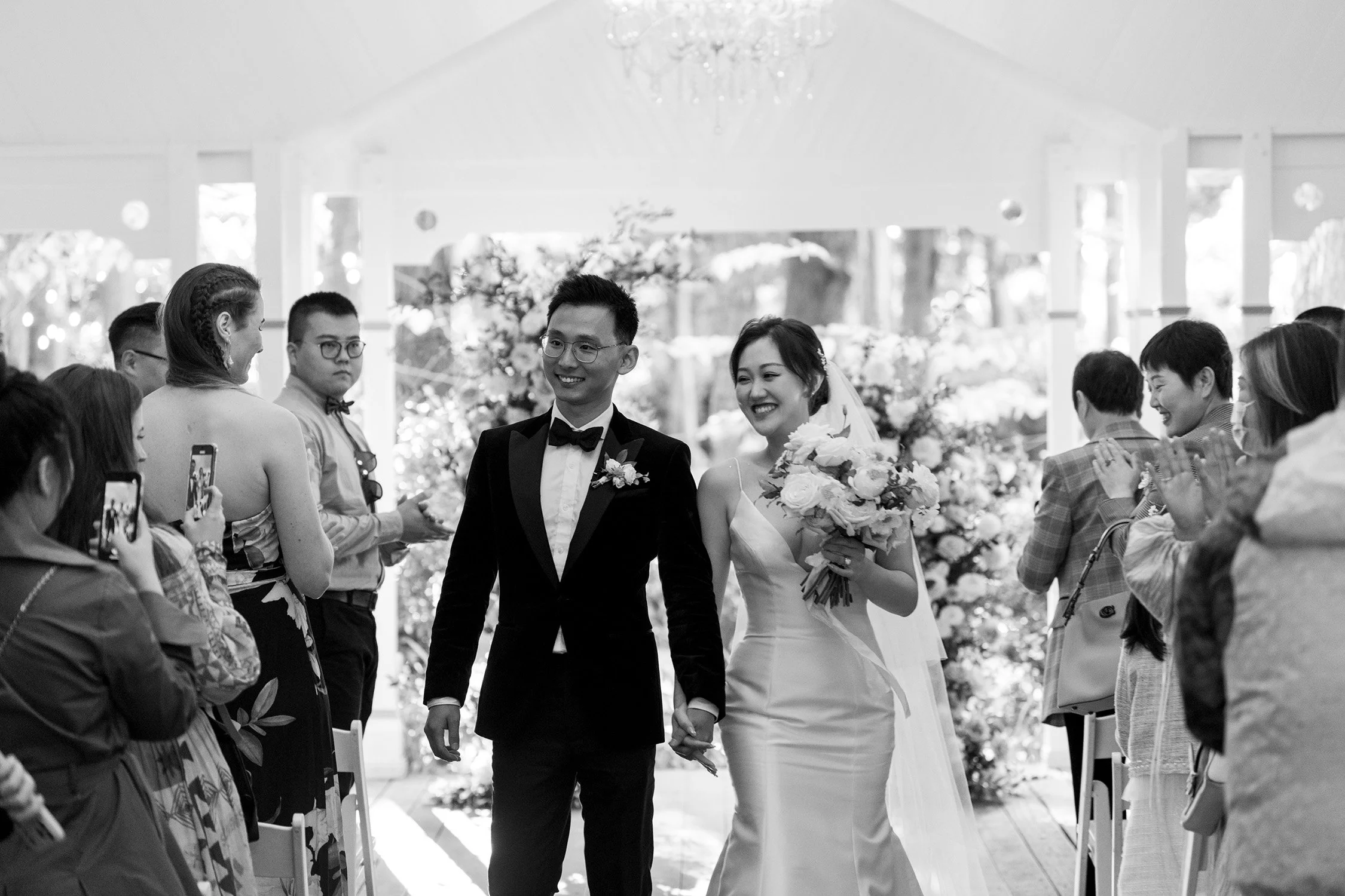bride and groom holding hands look at the guests walking down the aisle after wedding ceremony