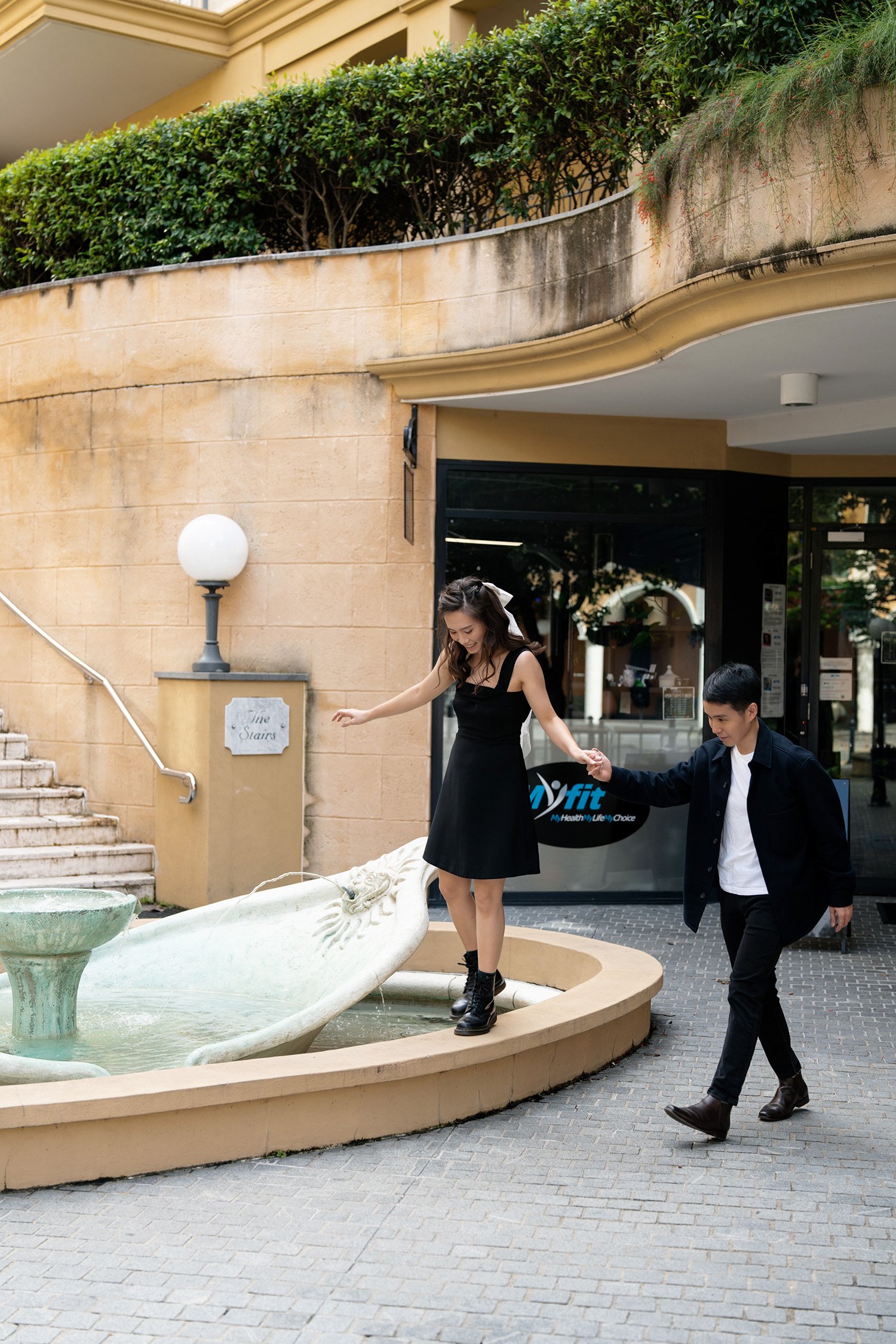 Paul and Krystel holding hands walking next to a fountain in their engagement photography session