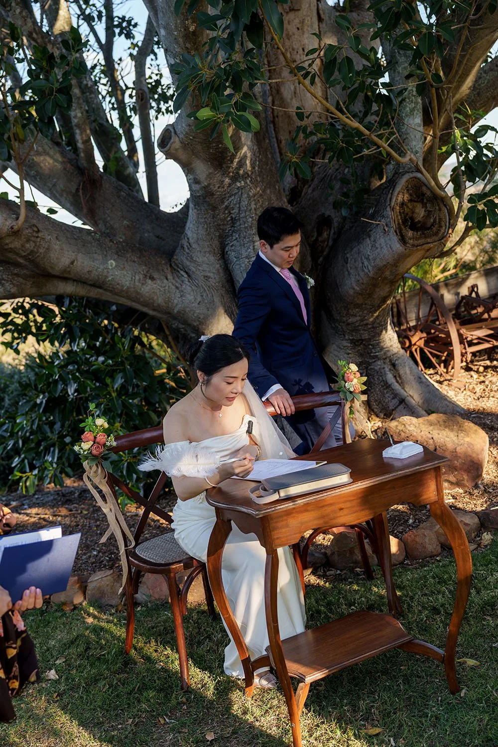 bride Flora signing the wedding registry document and Eric try to pull back his chair sitting