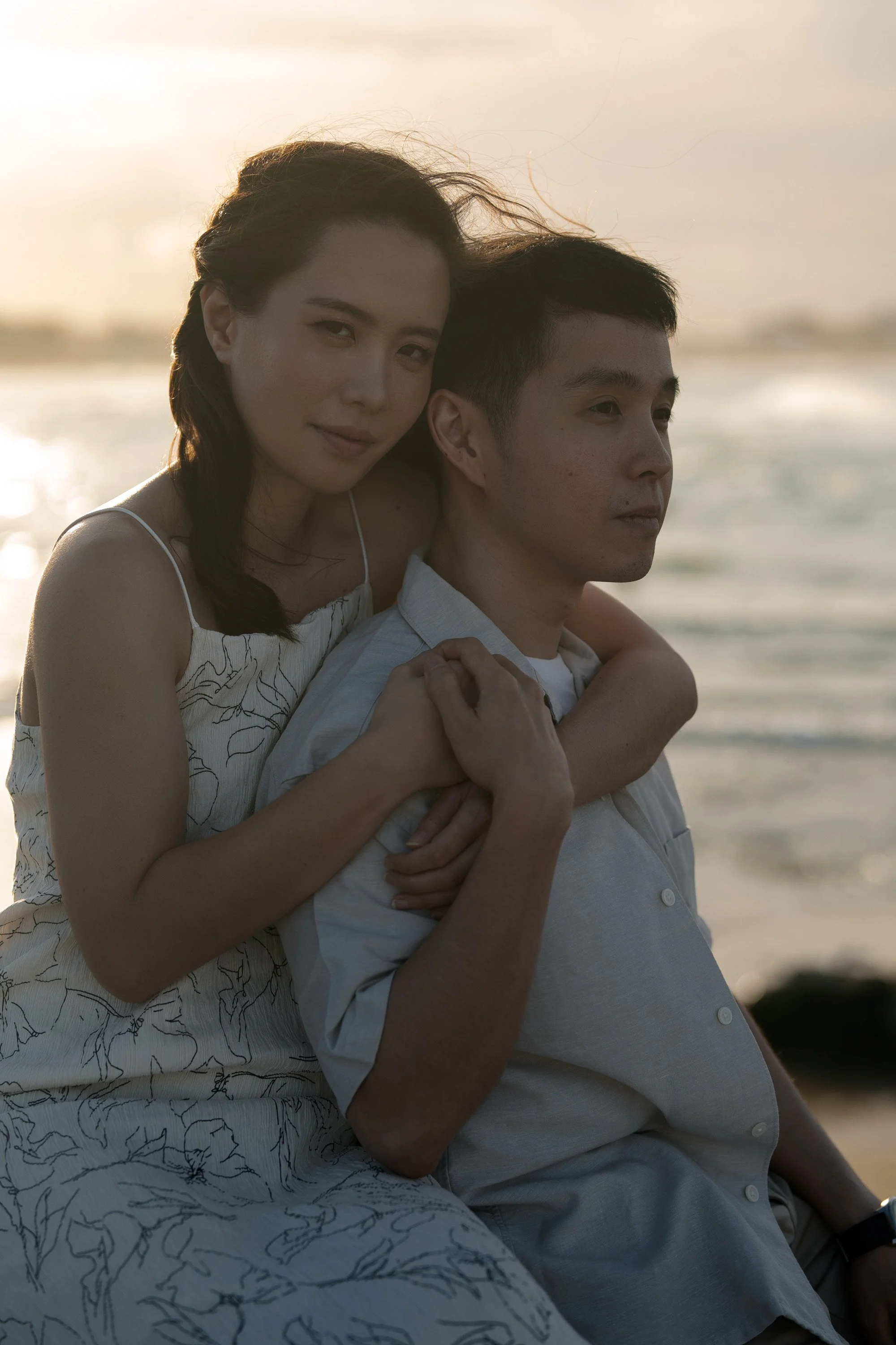 Krystel look at the Brisbane wedding photographer when holding Paul from back and they both setting in Currumbin Rock