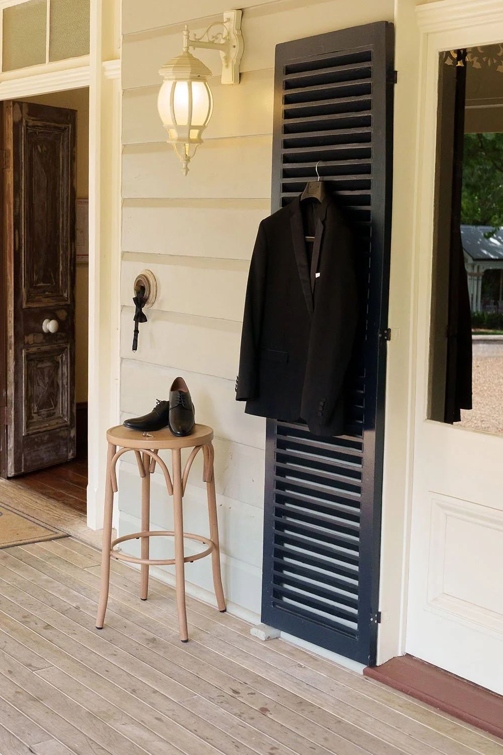 black jacket hanging on the black wooden sliding door, shoes and cufflink on top of a chair