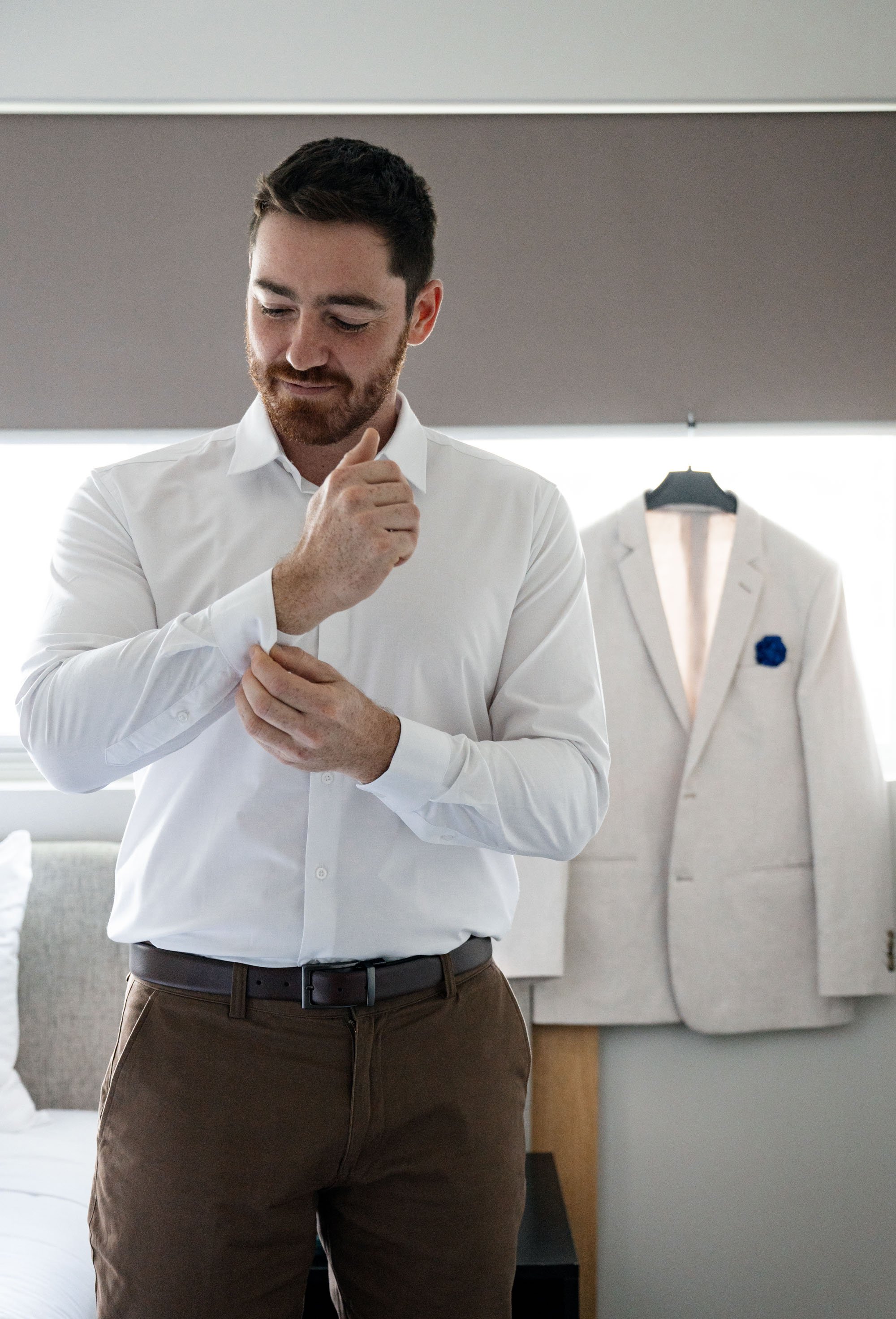 Groom Thomas adjusting his cufflink, adding a refined touch to his attire as he prepares for the wedding