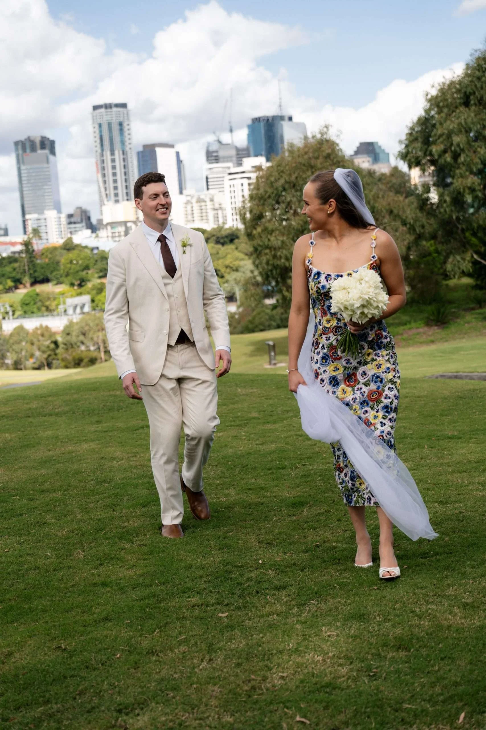 bride and groom look at each other while walking with Brisbane city background