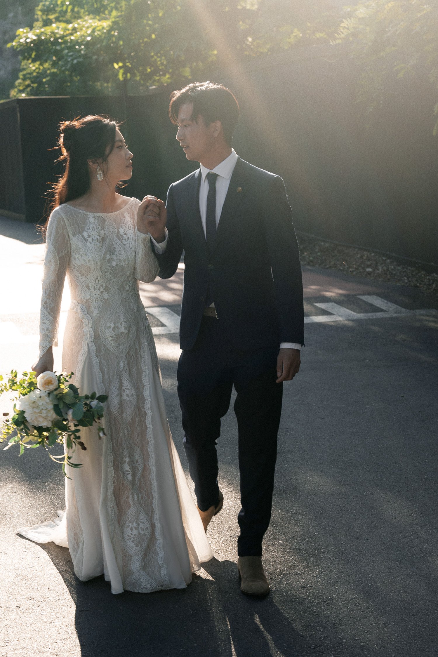 bride and groom holding hands look at each other when walking together with backlight