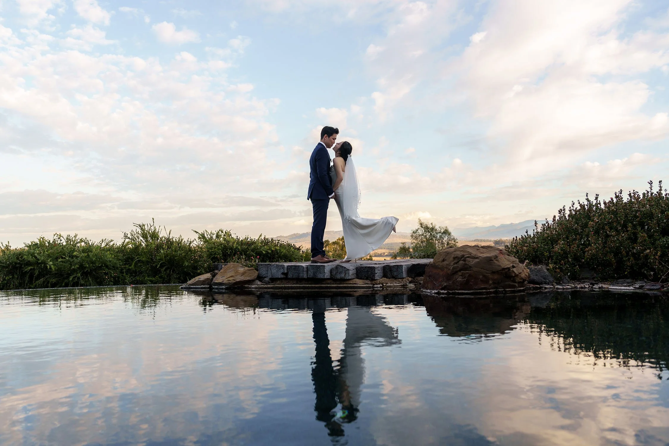 Eric and Flora kissing, and Flora banning her feet, they both stand on a wooden stage next a water pool
