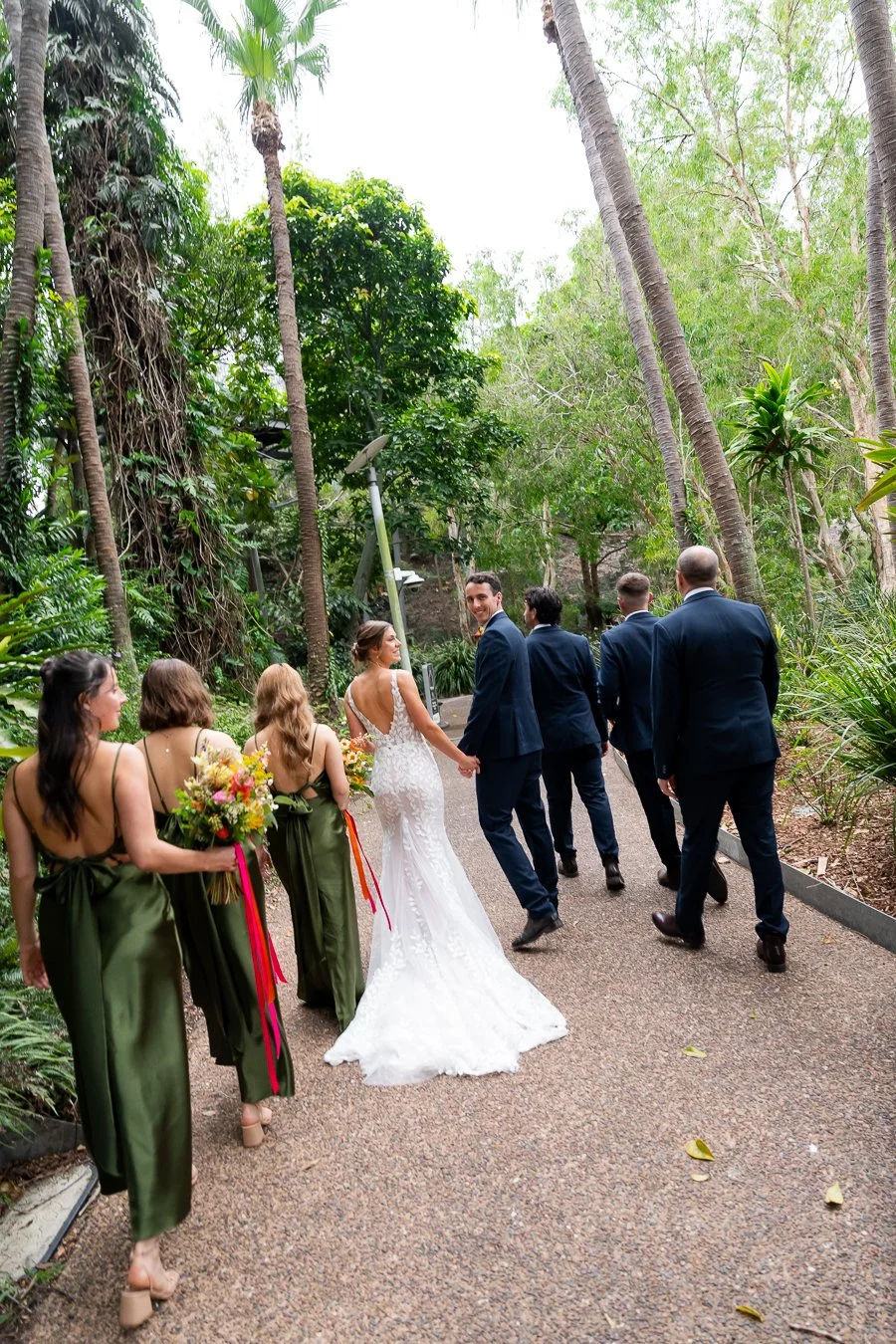 The groomsmen and bridesmaids walk together, with the bride and groom in the middle, looking back at the Brisbane photographer Whistler Li