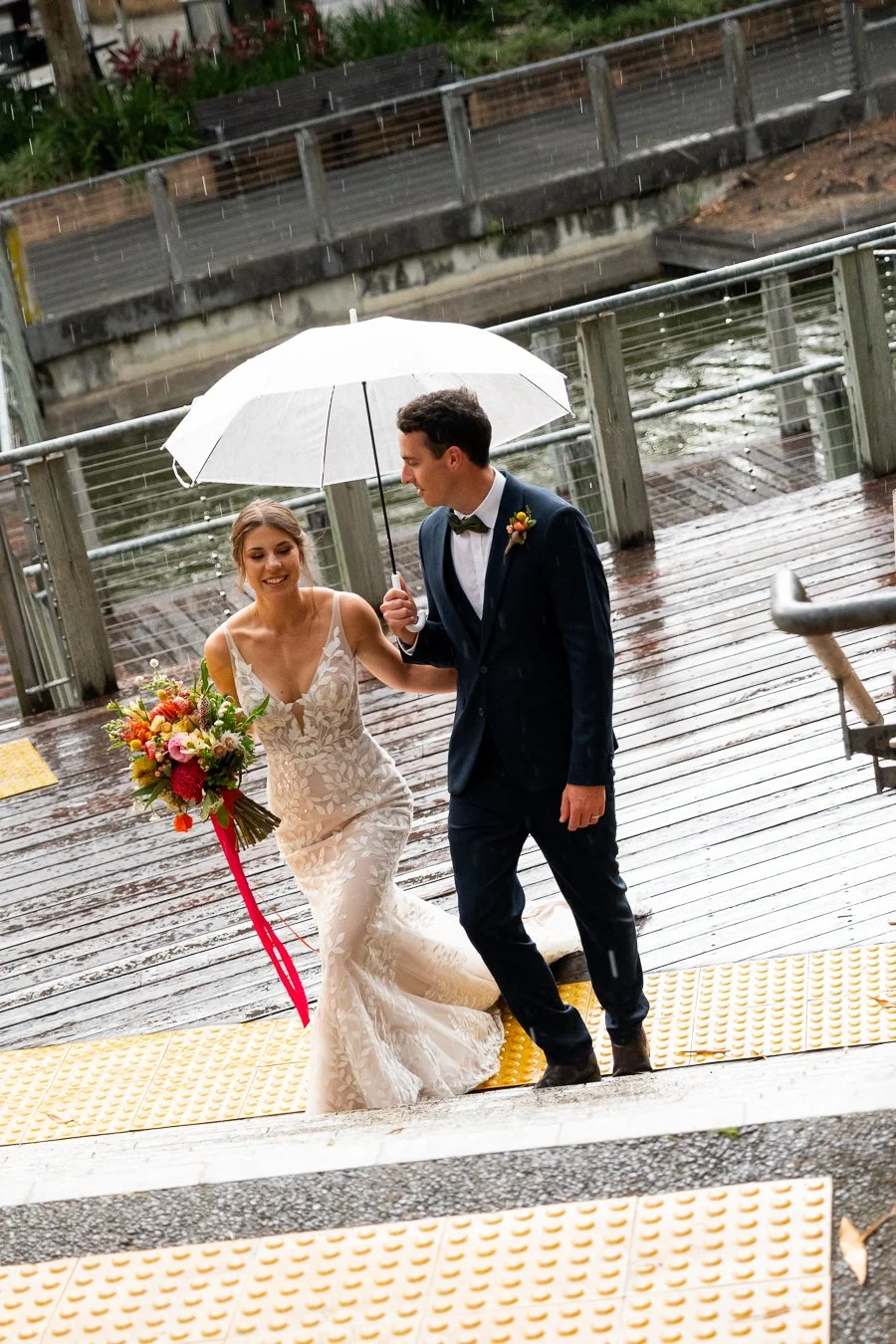 bride and groom walk on the stairs with groom holding umbrella in a raining day