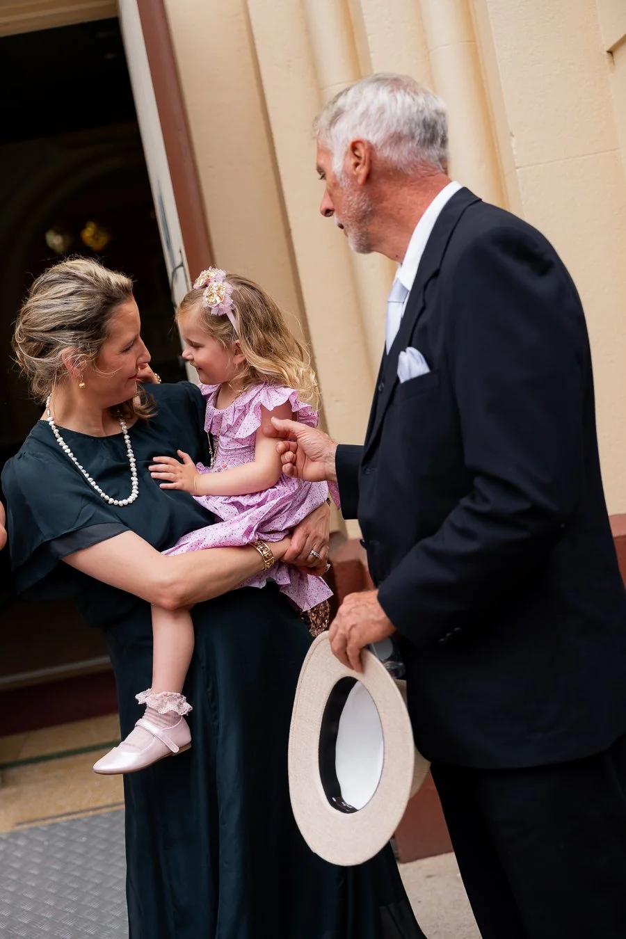 a female lady holding a baby girl and groom father next to them