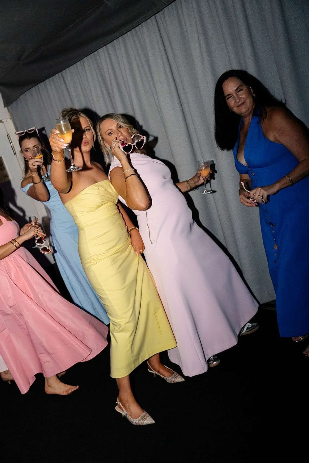 Four female guests holding glasses and sunglasses, cheering toward the camera.