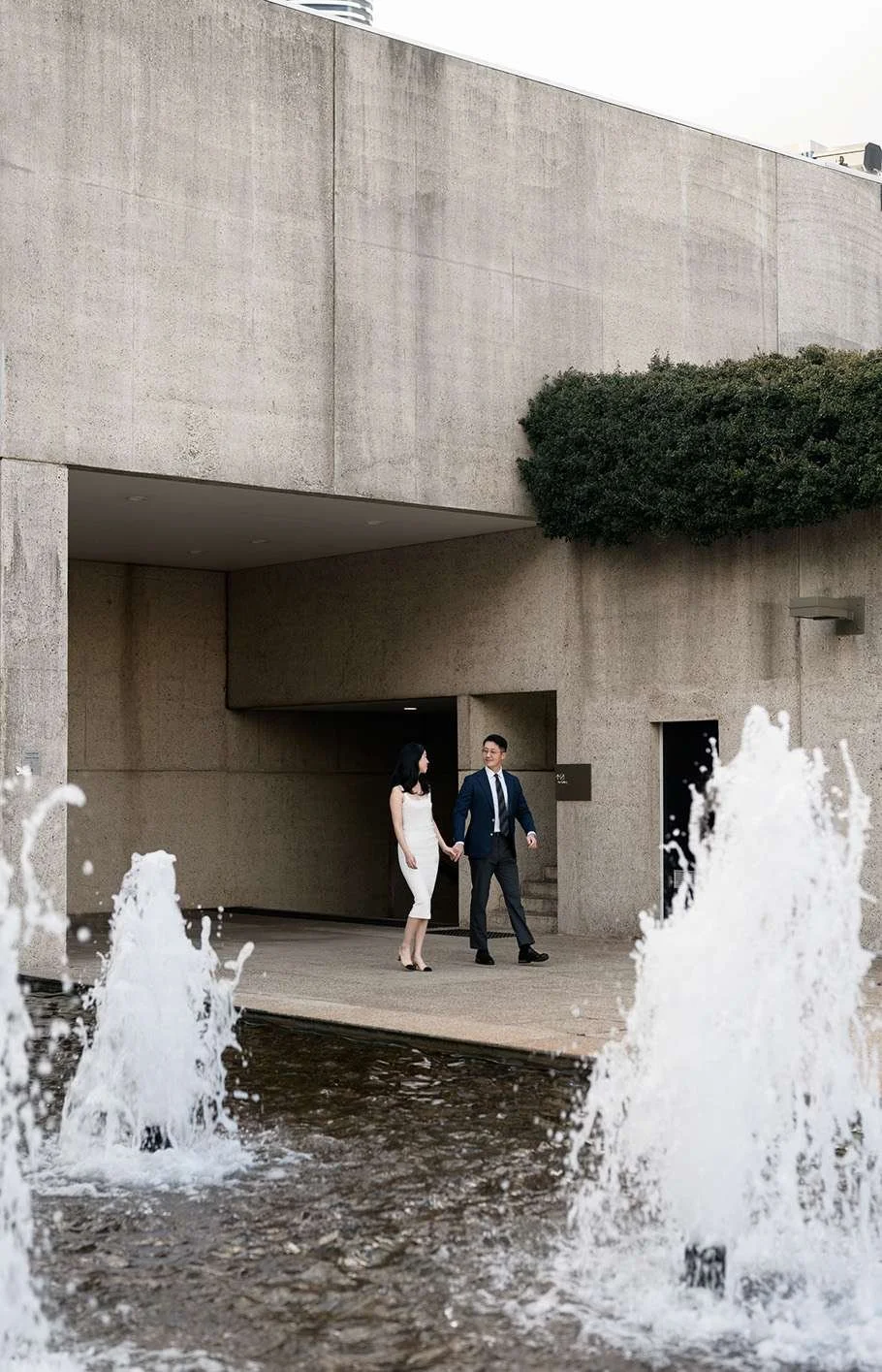 Bride and groom walking side by side next to a fountain in the Gallery of Art Museum, surrounded by the tranquil ambiance and stunning architecture, creating a romantic and timeless moment