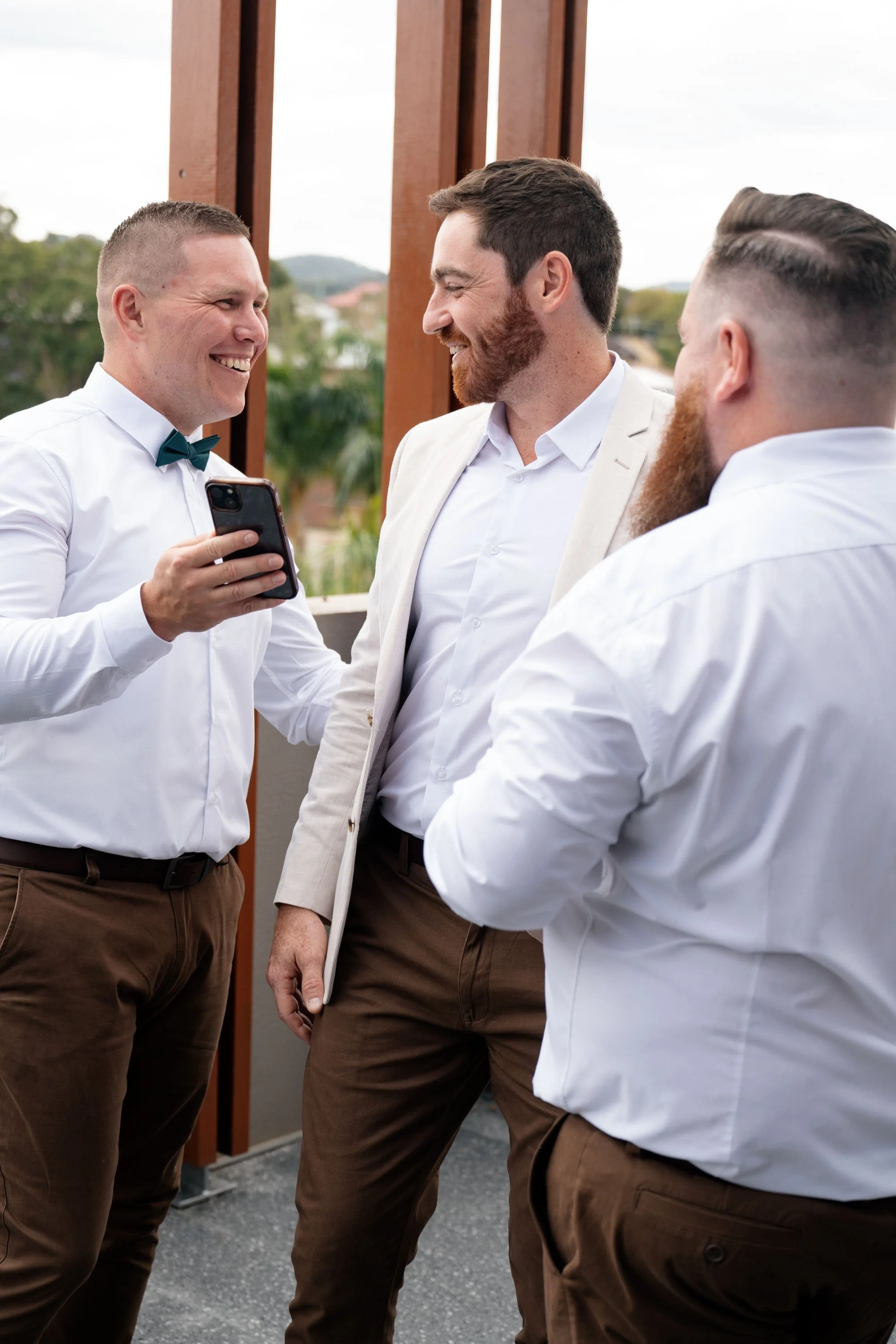 One of the groomsmen showing the iPhone screen to groom Thomas, sharing a moment of excitement or humor during the wedding day