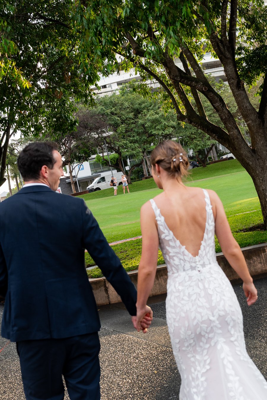 sun hits bride Sonya's face and she holding Giordan;s hand walking away from the Brisbane wedding photographer Whistler