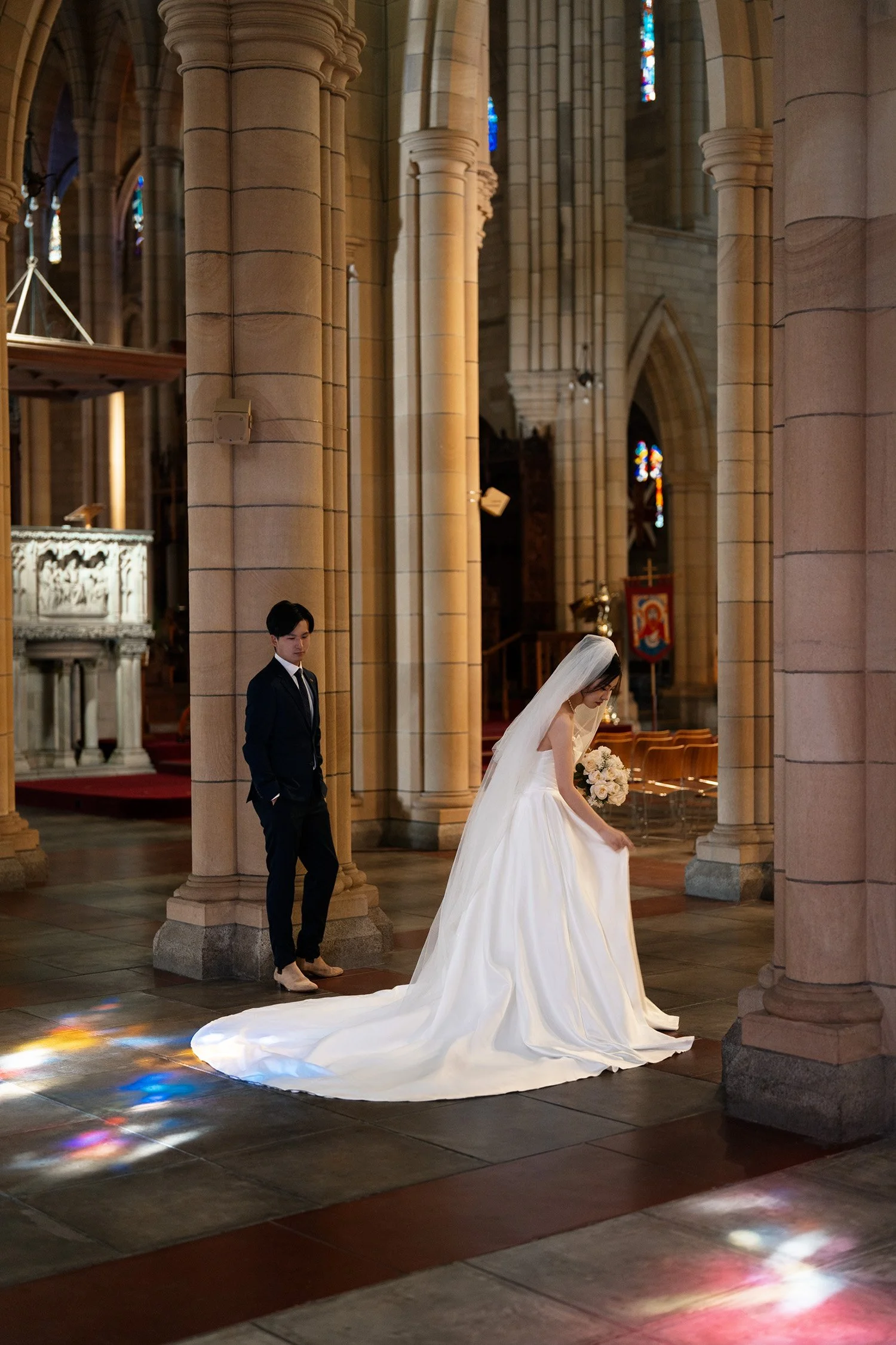 bride Cassie look down and adjust her dress and groom look at her dress in St John's Cathedral in Brisbane
