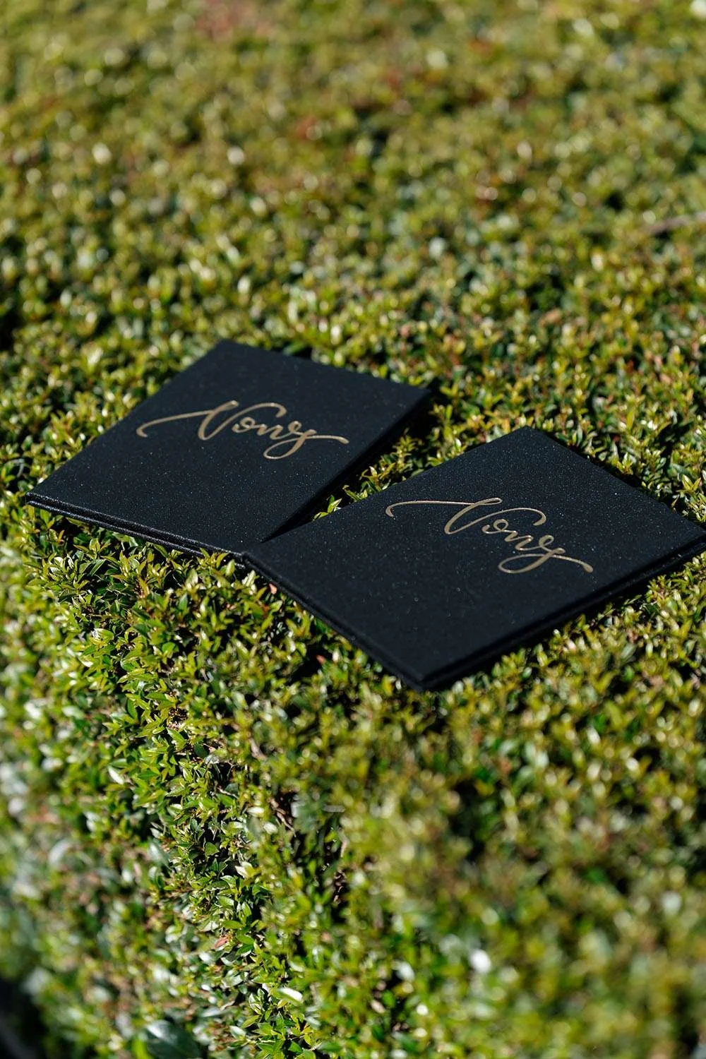 Bride and groom vow booklets resting on green bush leaves during outdoor wedding