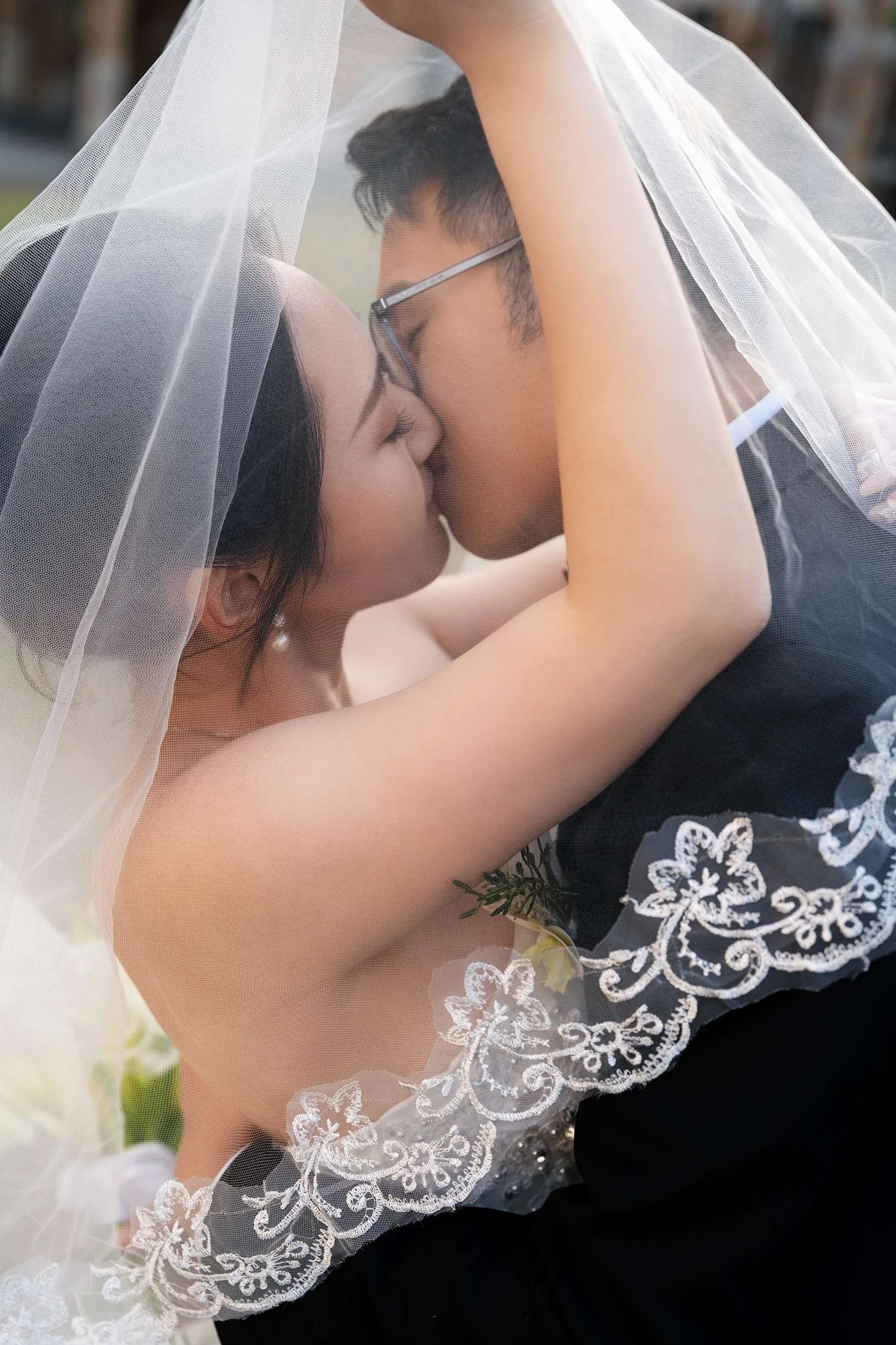 Bathan and Peter close eyes kissing under her veil while doing their location shoot at THe University of Queensland