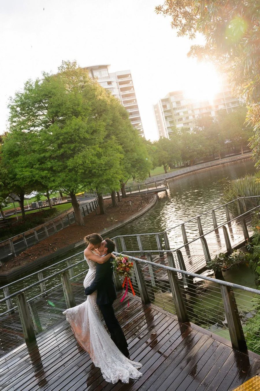 groom Giordan lifting bride Sonya up and kissing in Roma street parkland with sun out after running