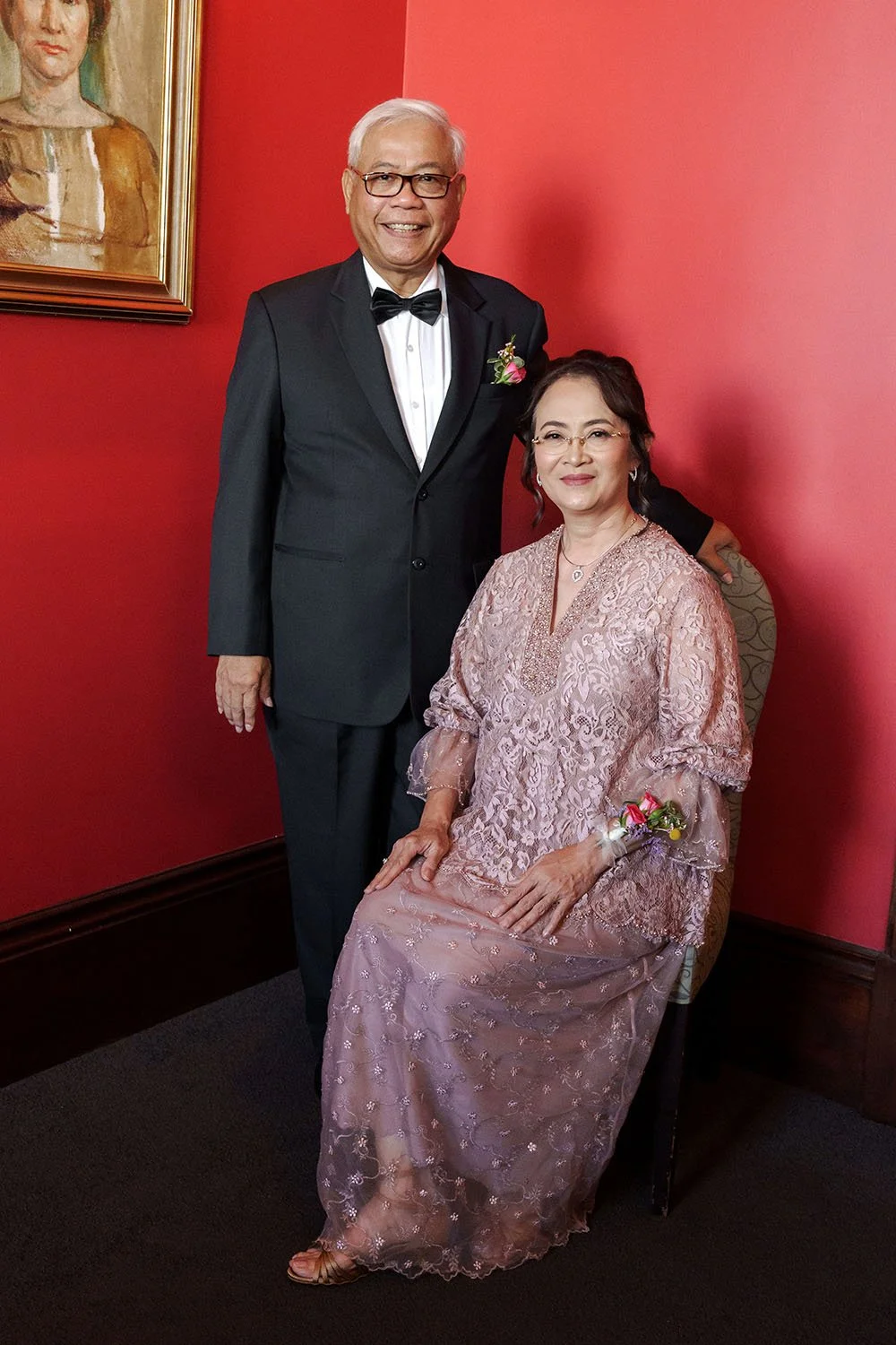 bride Nori's parents, mum sitting on the chair and father stand next to her