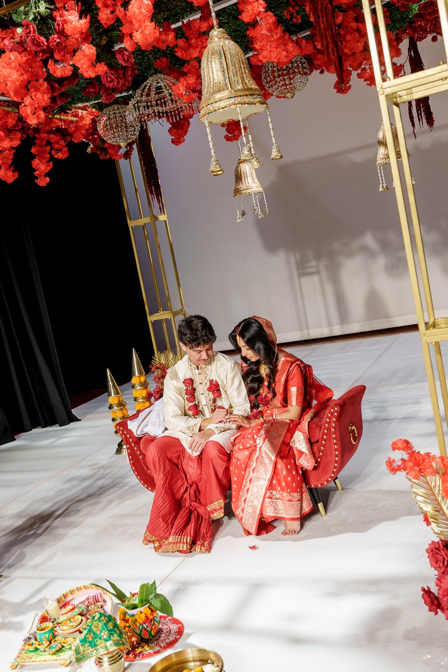 Amrita and Casey both look at the engagement ring when they both sitting on a red sofa