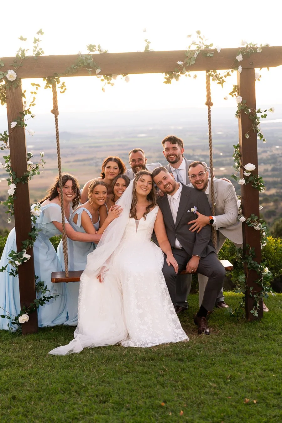 Chiarra and Ben sitting on the swing and all the bridal party holding them from back