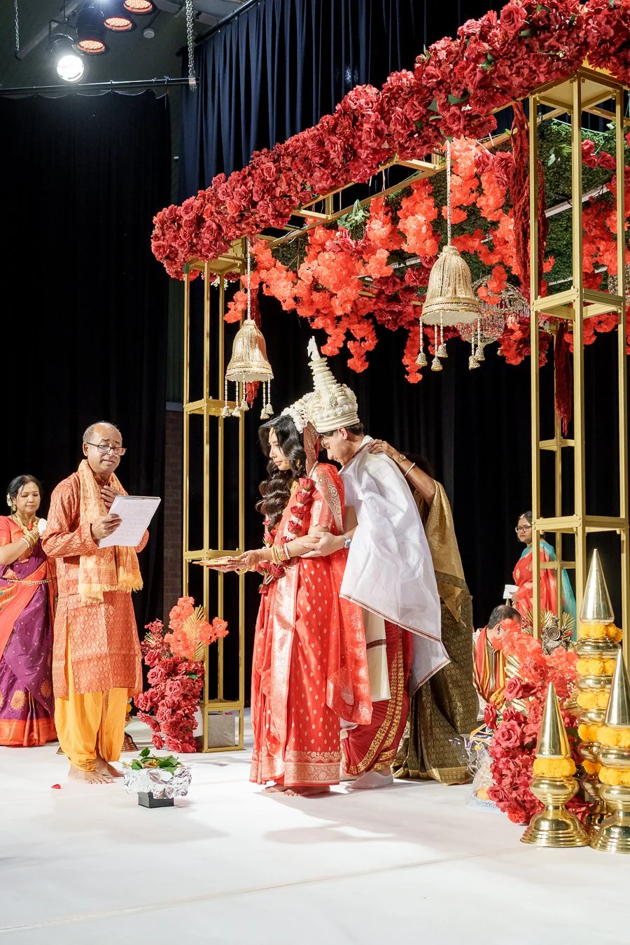 Casey holding Amrita from back, his mother in law stand next to the priest