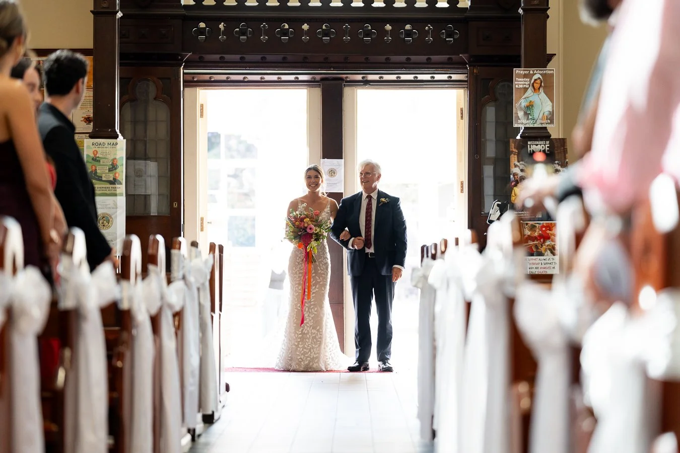 The bride, arm in arm with her father, stood at the doorway, smiling at their guests