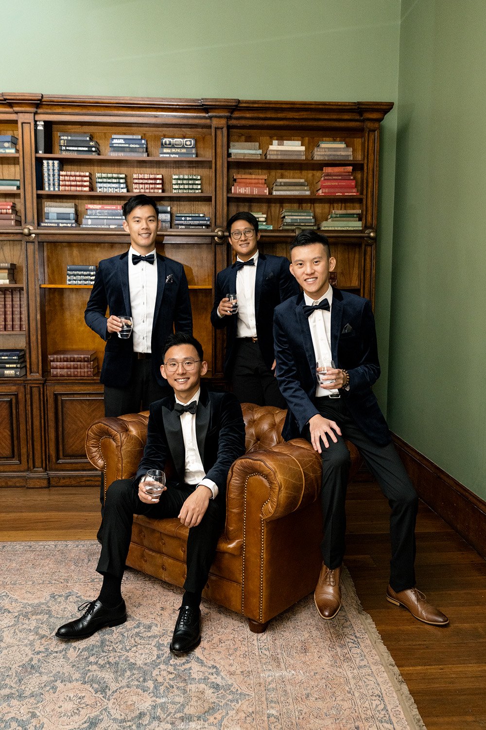 groom Brus sitting on the sofa and groom's men standing next to him, all look at the Brisbane wedding photographer Whistler