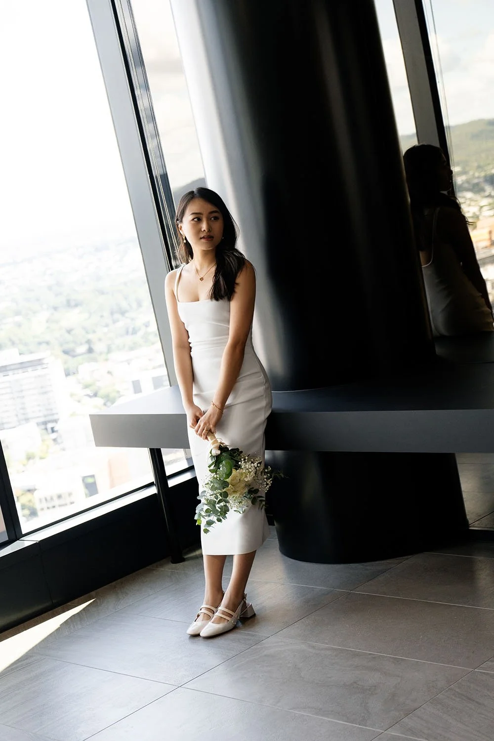 Michelle leaning on the table look in her fitted white wedding dress inside the hallway