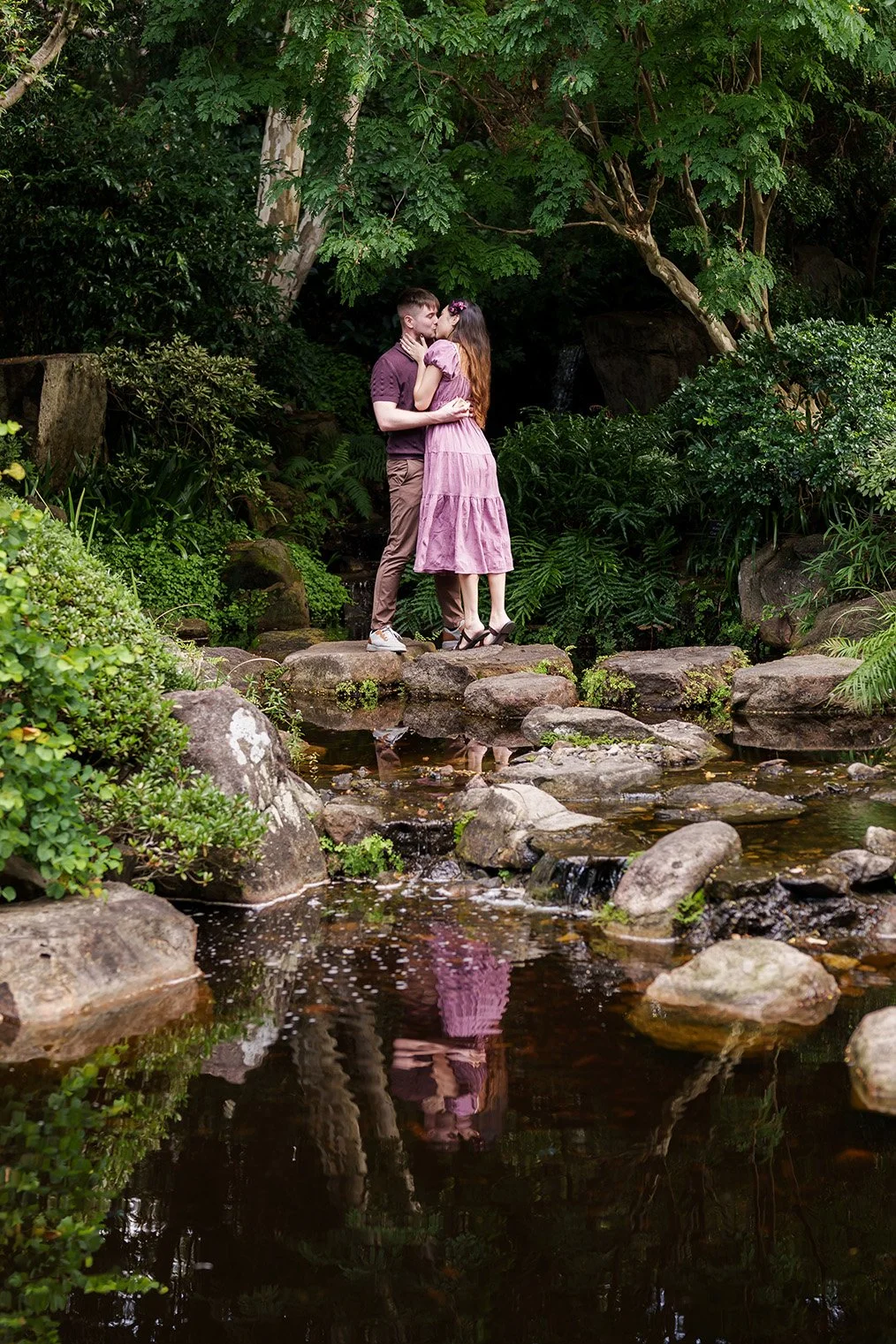 Ruby and Kyle kissing on rocks, next to a lake in Brisbane Botanic Gardens Mt Coot-tha