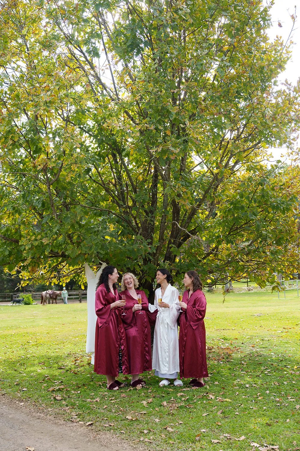 Jasmin and her bride mates talking and laughing under a maple tree next to her dress