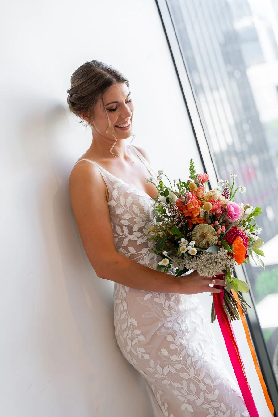 The bride leaned against the wall, looking down at the flowers