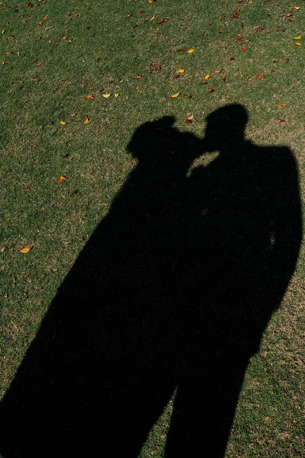 Bride and groom kissing with their shadow cast on the grass during a wedding location shoot