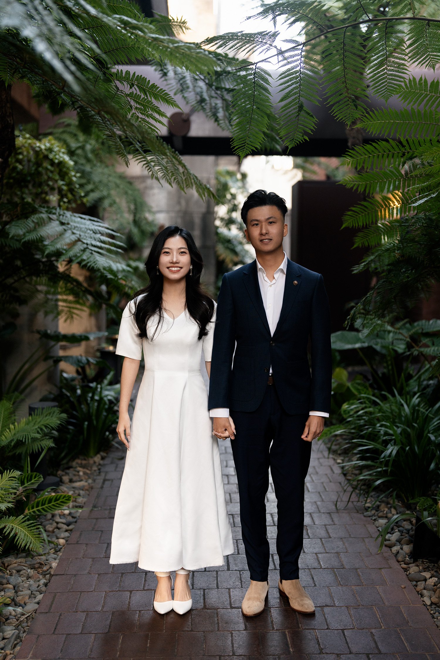 bride and groom look at the Brisbane engagement photographer with smile when holding hands standing next to each other