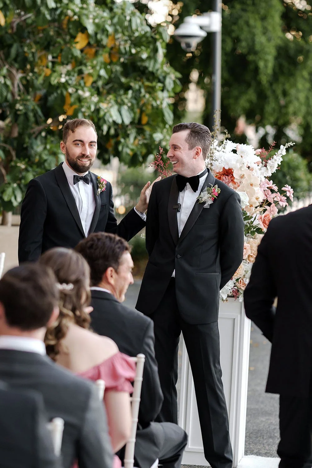 The groomsman pats the groom on the shoulder, whispering 'You've got this,' which brings a smile to the groom's face