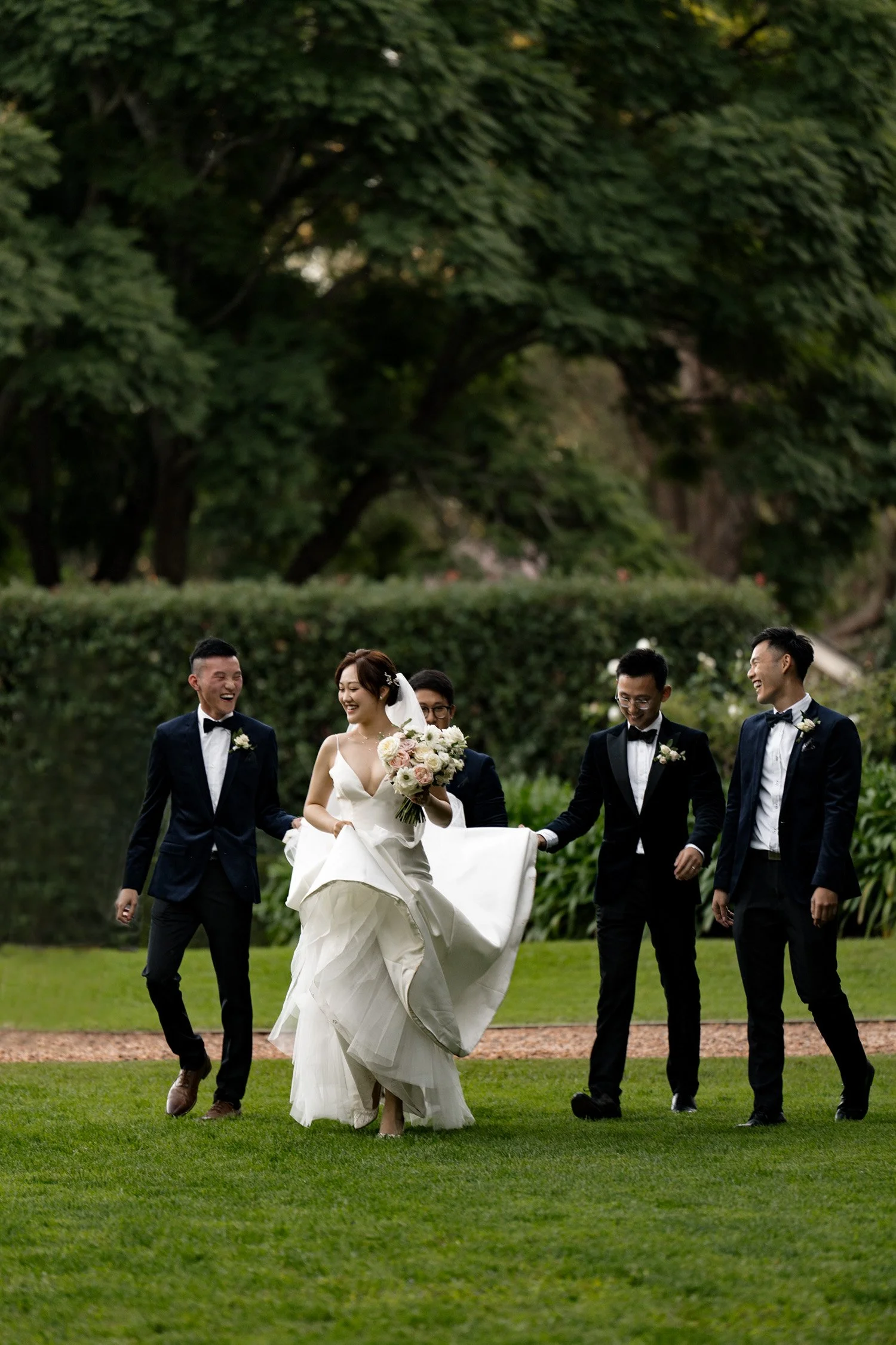 groom holding the tail of bride's dress and bride walking with groomsmen laughing and talking in Gabbinbar Homestead