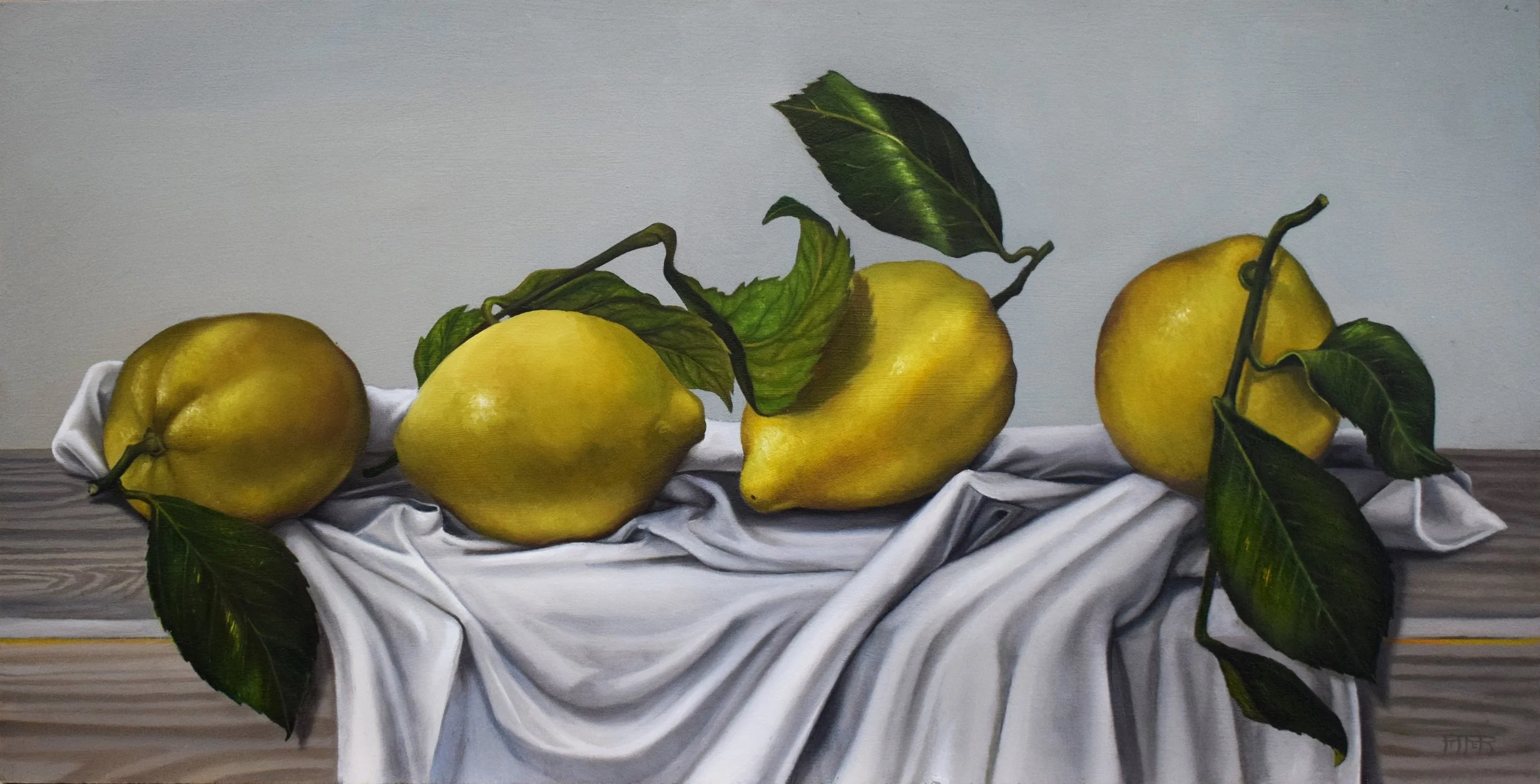 Four yellow pears with green leaves arranged on a white cloth on a wooden table, with a plain background.