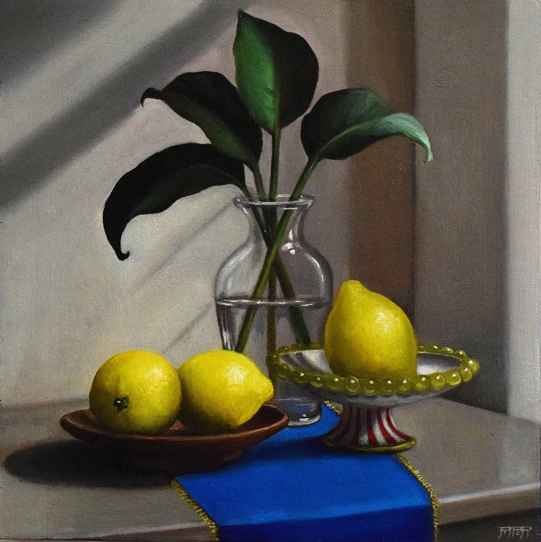 Still life arrangement of fresh lemons in a brown bowl, a glass vase with a branch of green leaves, and a yellow lemon on a decorative plate with a blue cloth and gold trim, set against a neutral background.