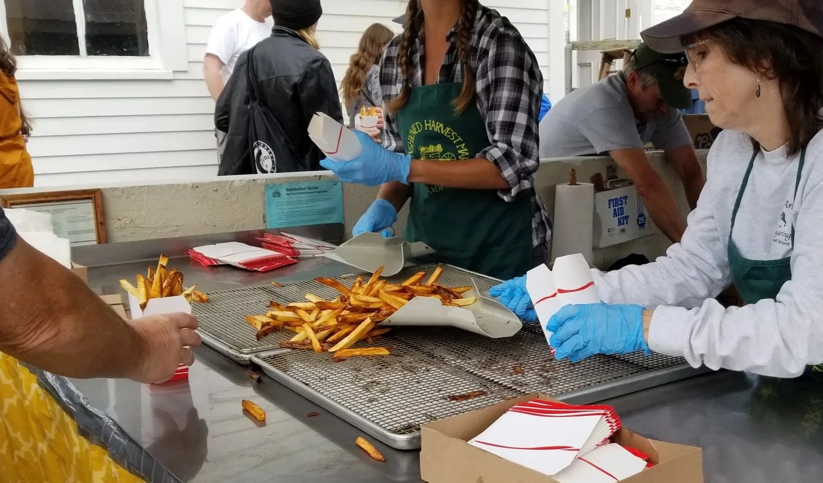 People serving and receiving fast food, specifically French fries, at an outdoor event.