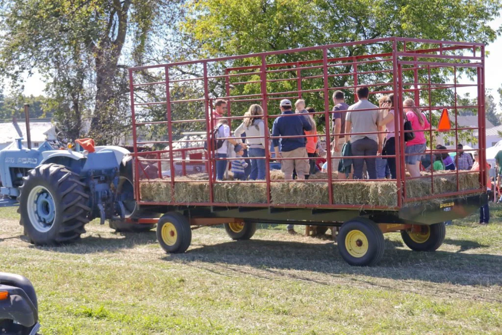 A tractor pulling a hayride wagon filled with people at an outdoor event.