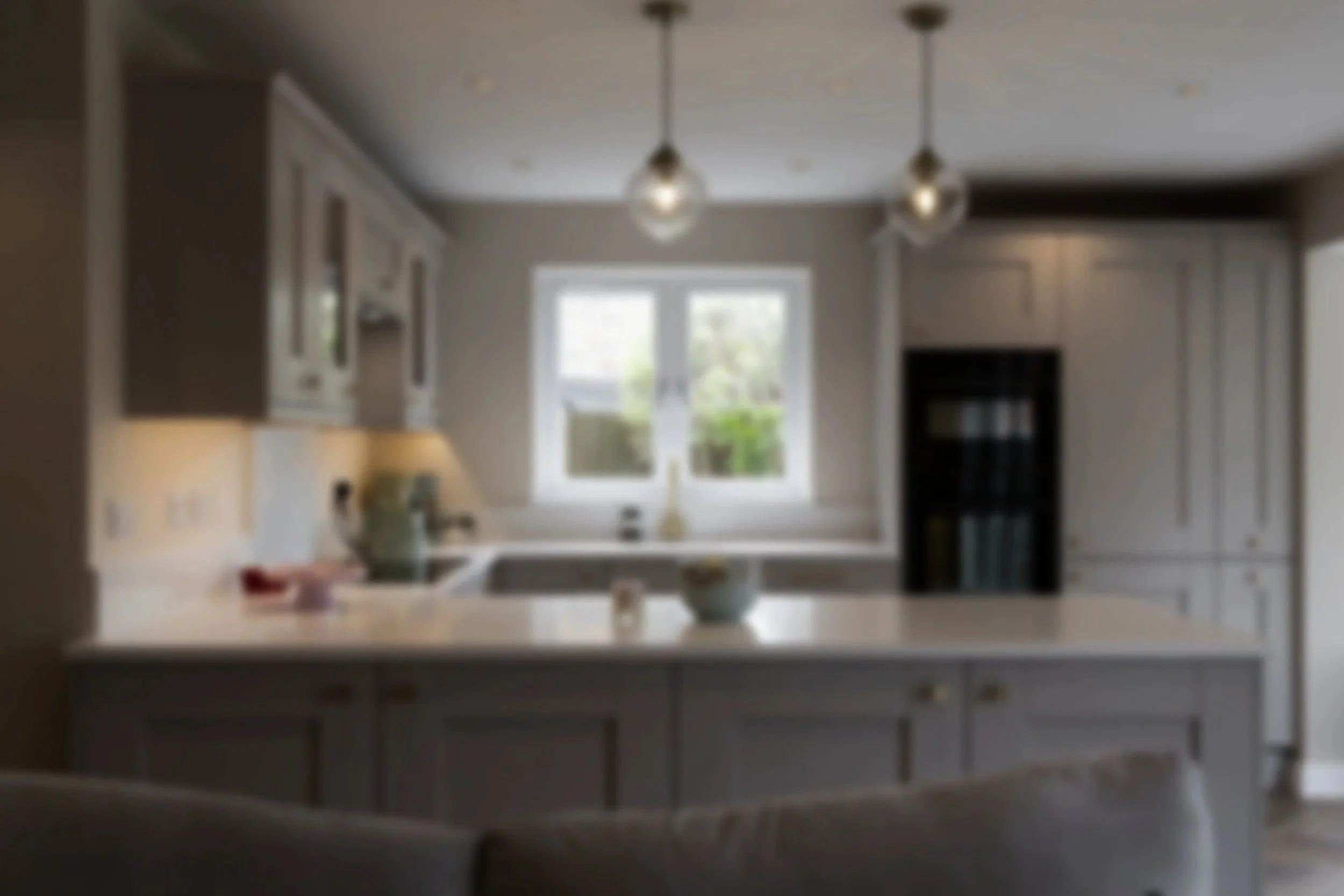 Blurry kitchen interior with white cabinetry, a window, and ceiling lights.