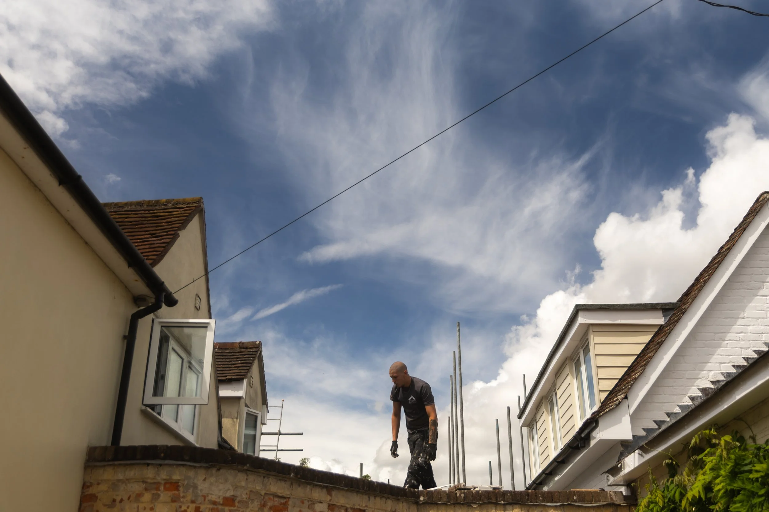 Man working on roofing of a house with cloudy sky in the background.