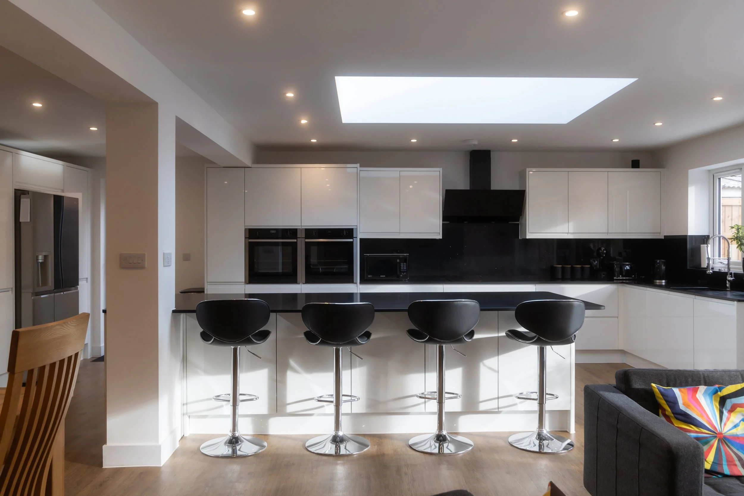 Modern kitchen with white cabinets, black countertops, a central island with black bar stools, and a skylight in the ceiling.