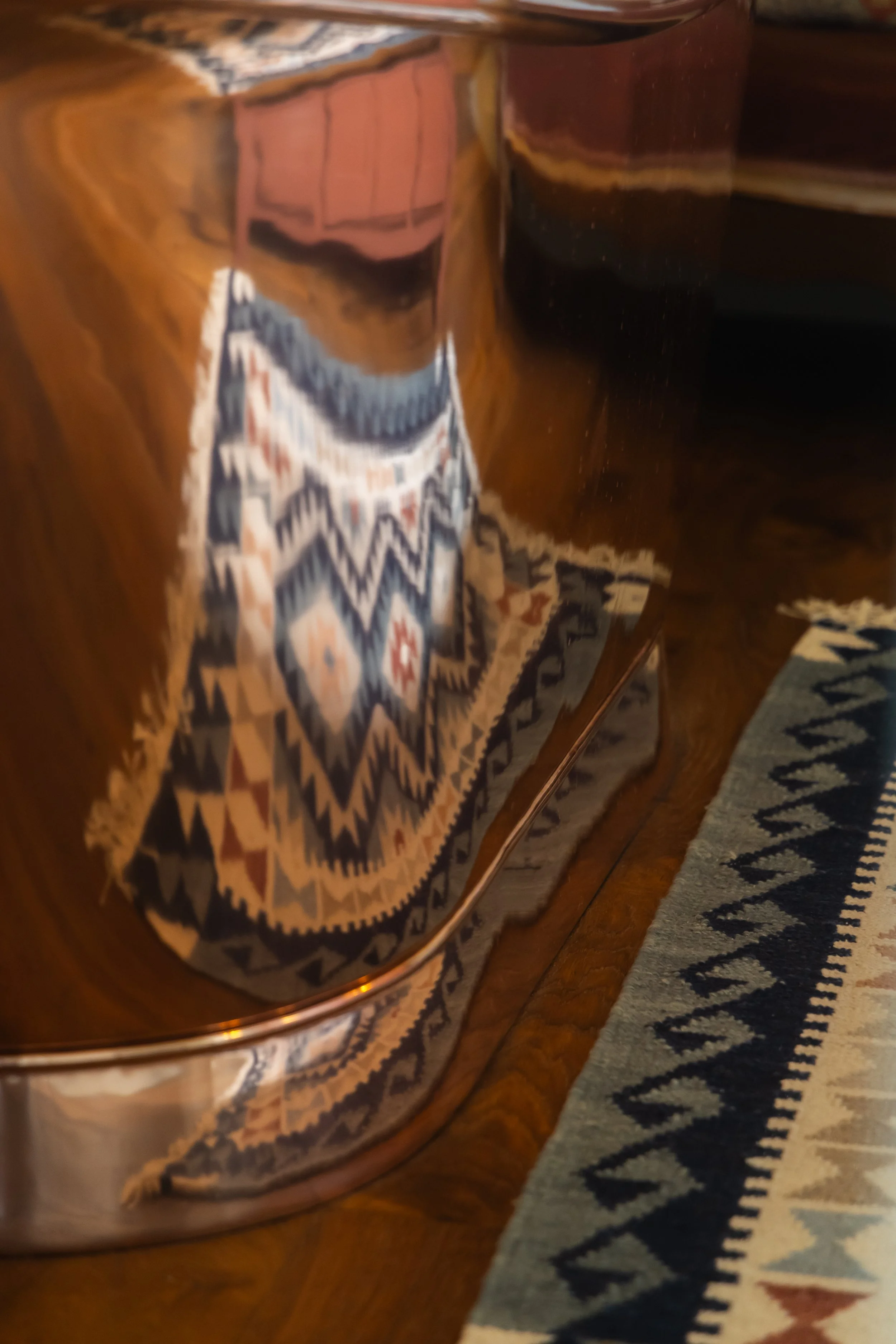 Reflection of a colorful patterned rug and some furniture in a shiny, curved wooden surface.