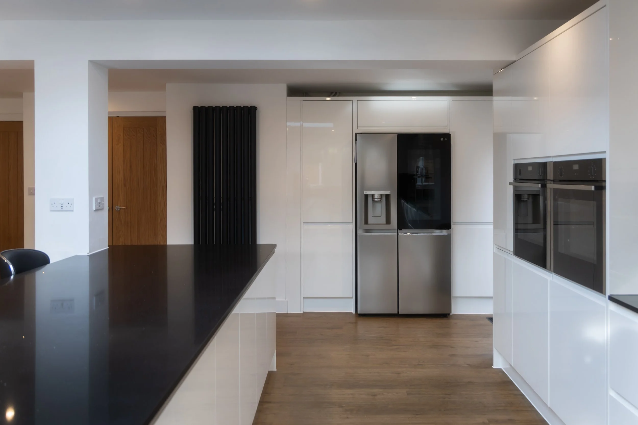 Modern kitchen with white cabinets, black countertop island, stainless steel refrigerator, wall ovens, and wooden flooring.
