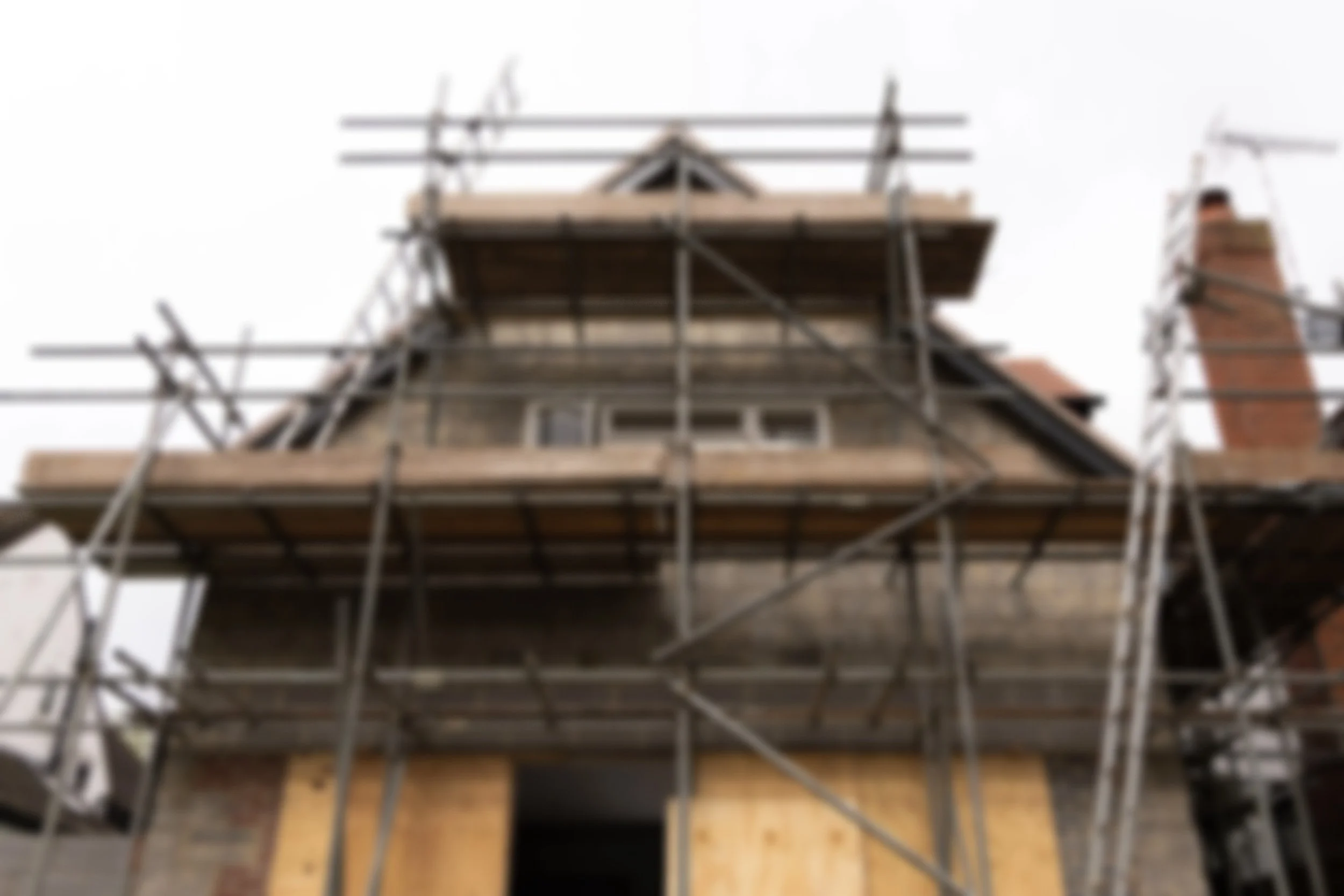 Construction scaffolding surrounding a house under renovation, with visible chimney and roof structure.
