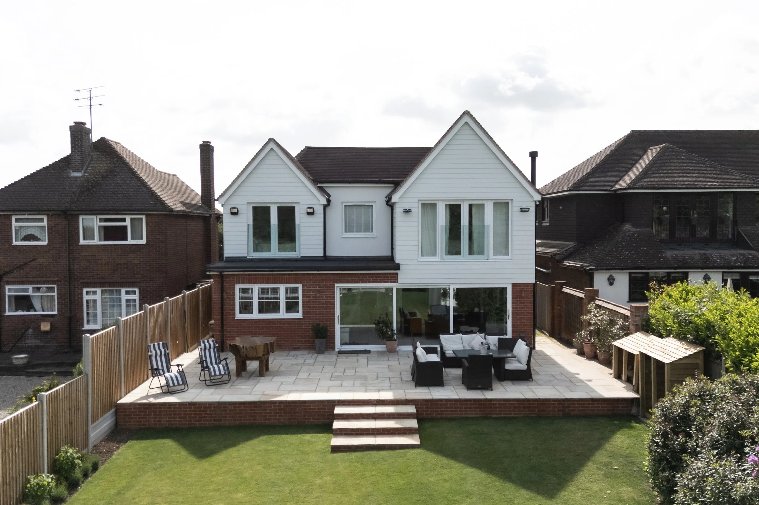 Backyard with patio area, outdoor furniture, and well-maintained grass yard, surrounded by wooden fences and neighboring houses