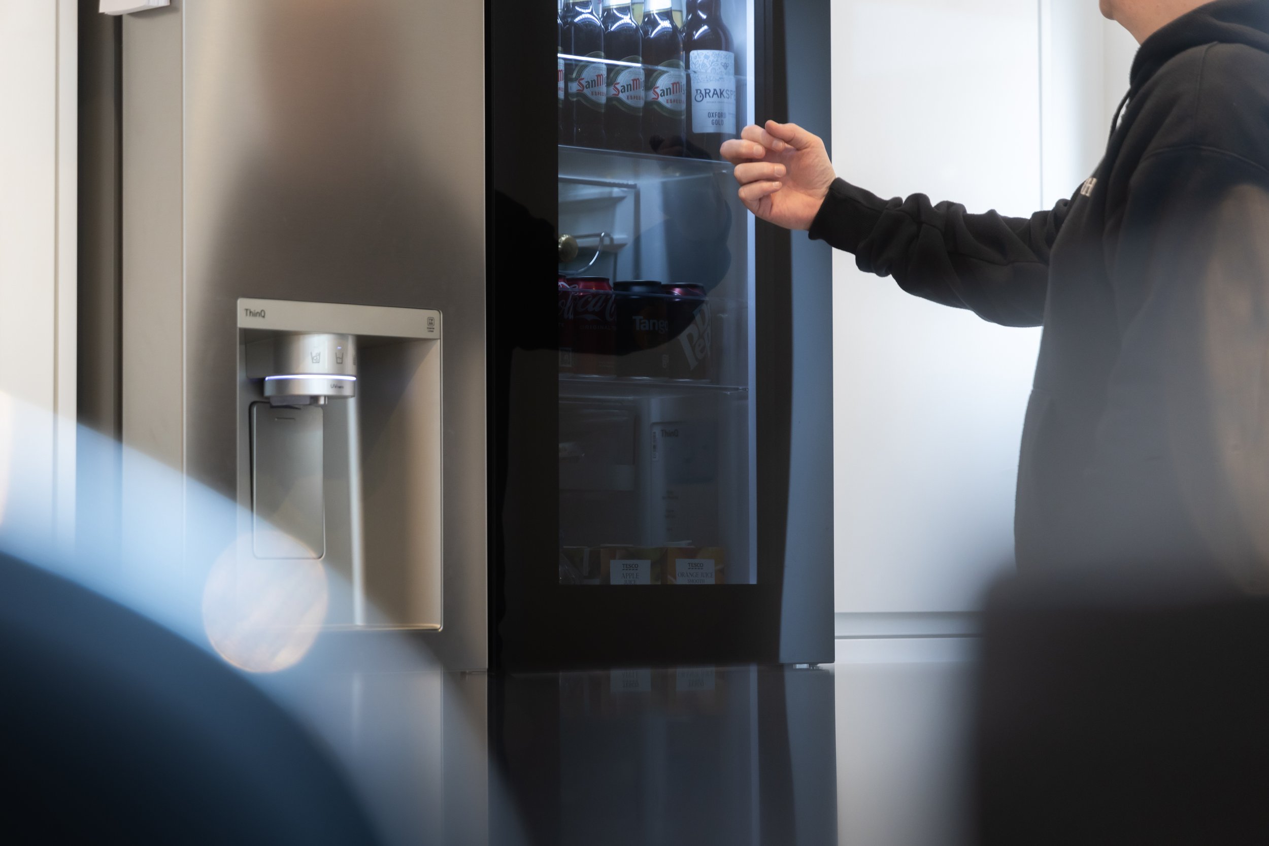 Person opening a glass door on a beverage refrigerator, which contains bottled drinks, with the person's face not visible.