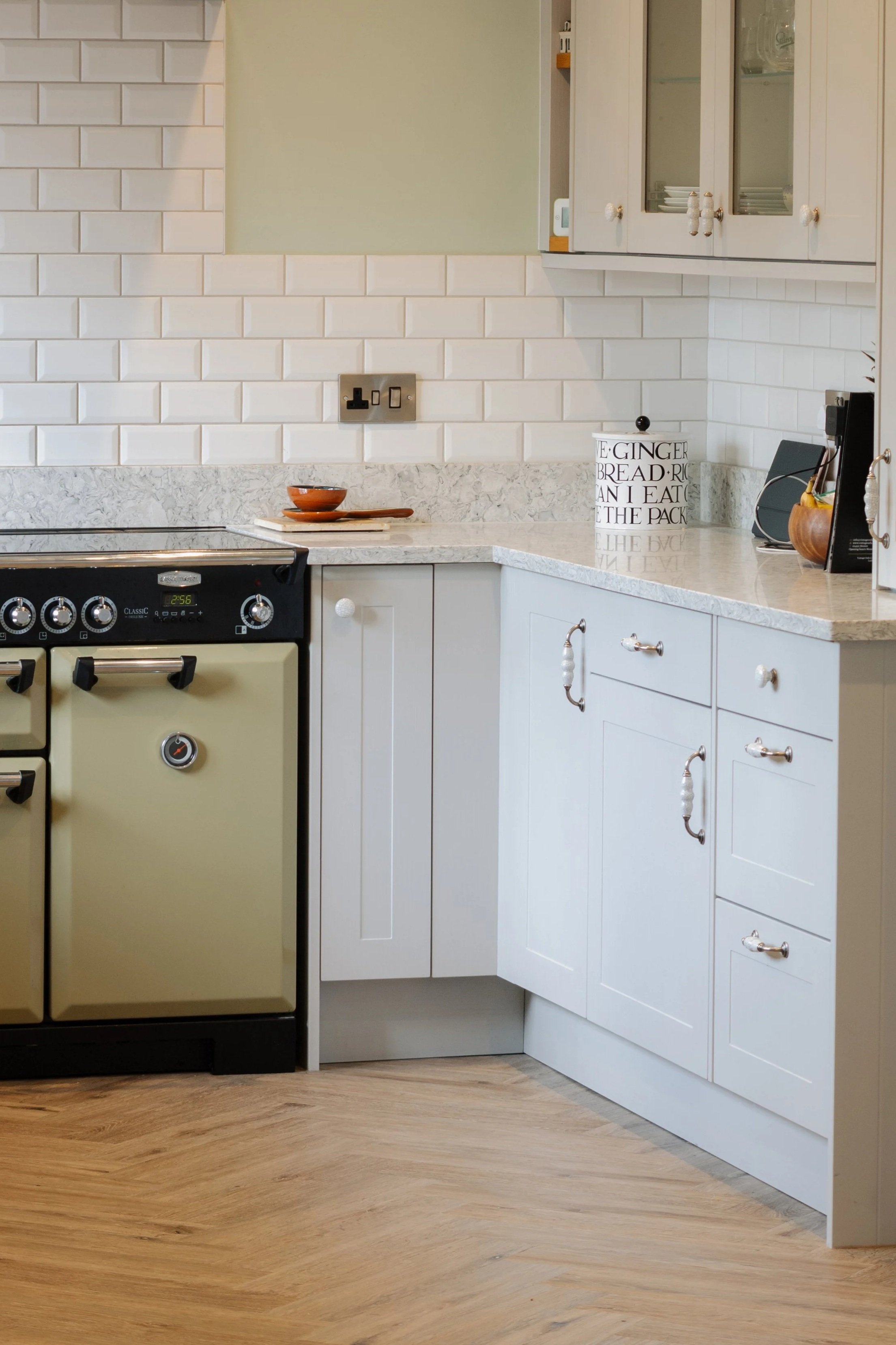 Kitchen with white cabinets, a marble countertop, a vintage cream-colored oven, a white jar with black text, and wooden flooring.