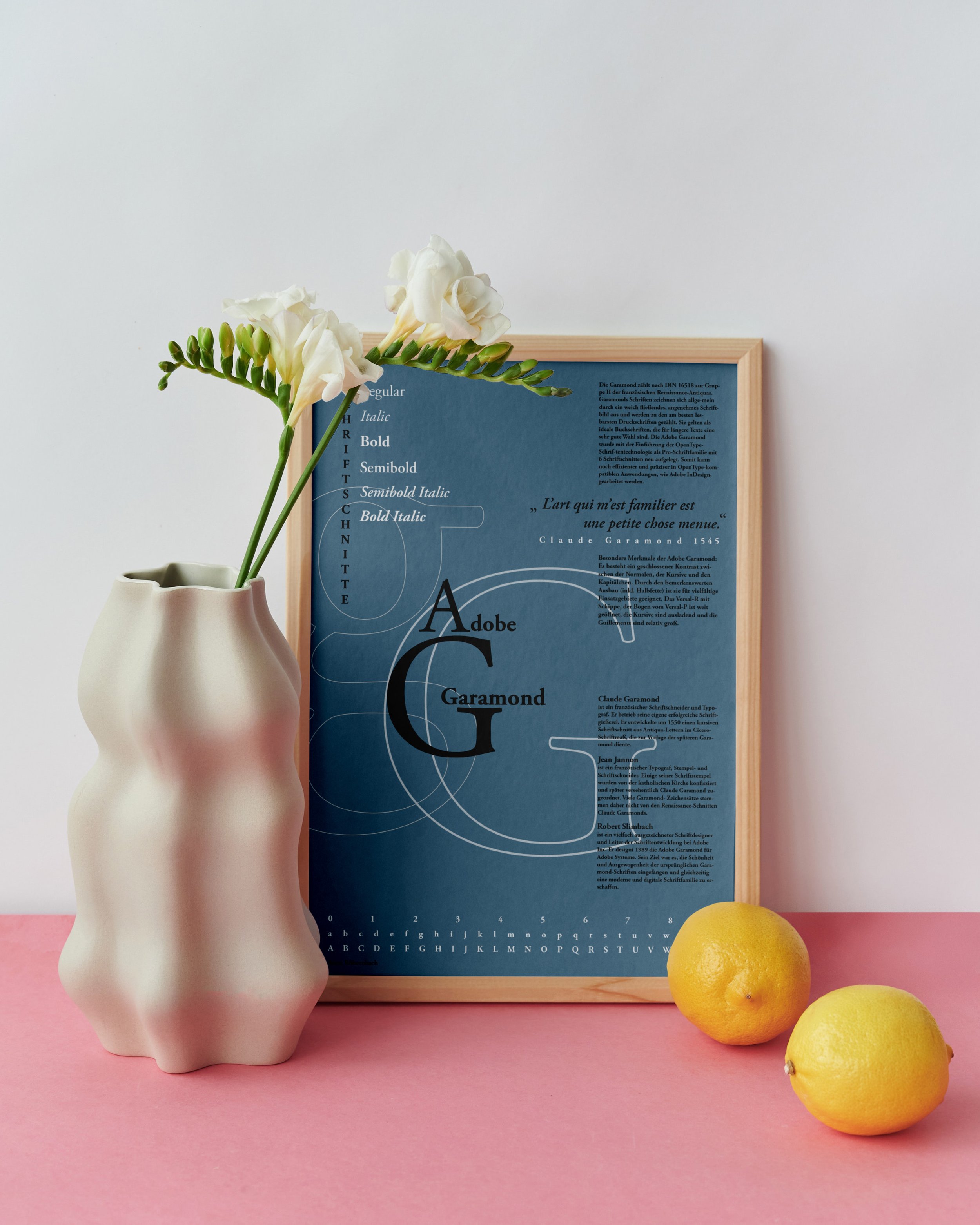 Eine weiße Vase mit zwei weißen Blumen, drei Zitronen und einem blauen gerahmten Poster auf einem rosa Hintergrund.