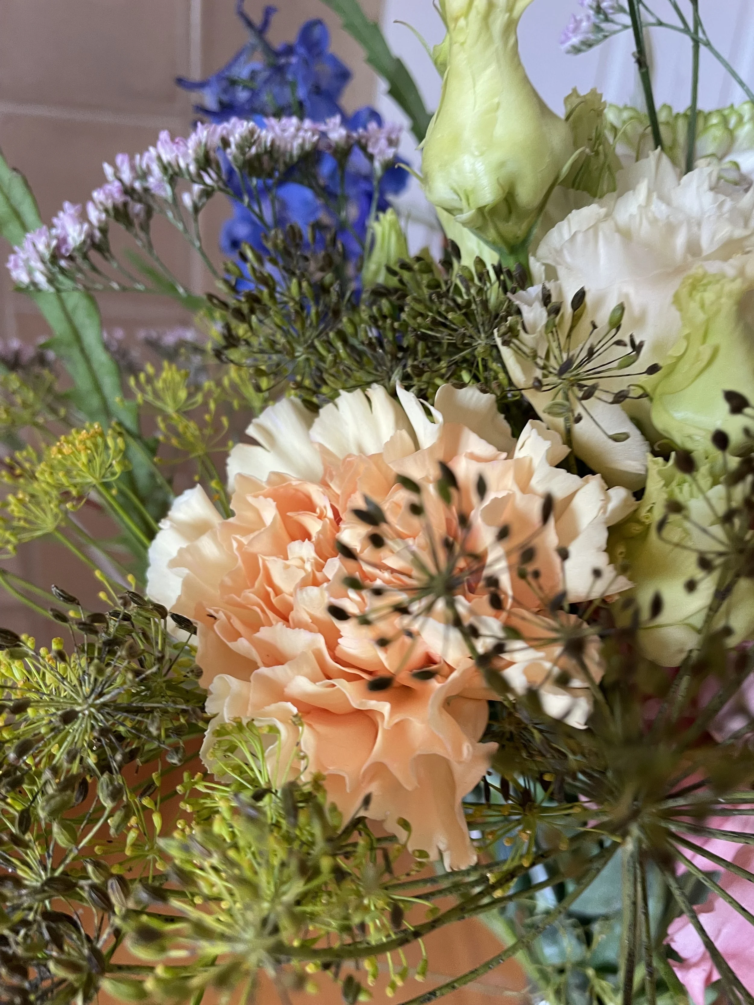Blumenstrauß mit hellpinken, weißen, blauen und grünen Blumen und Blättern.